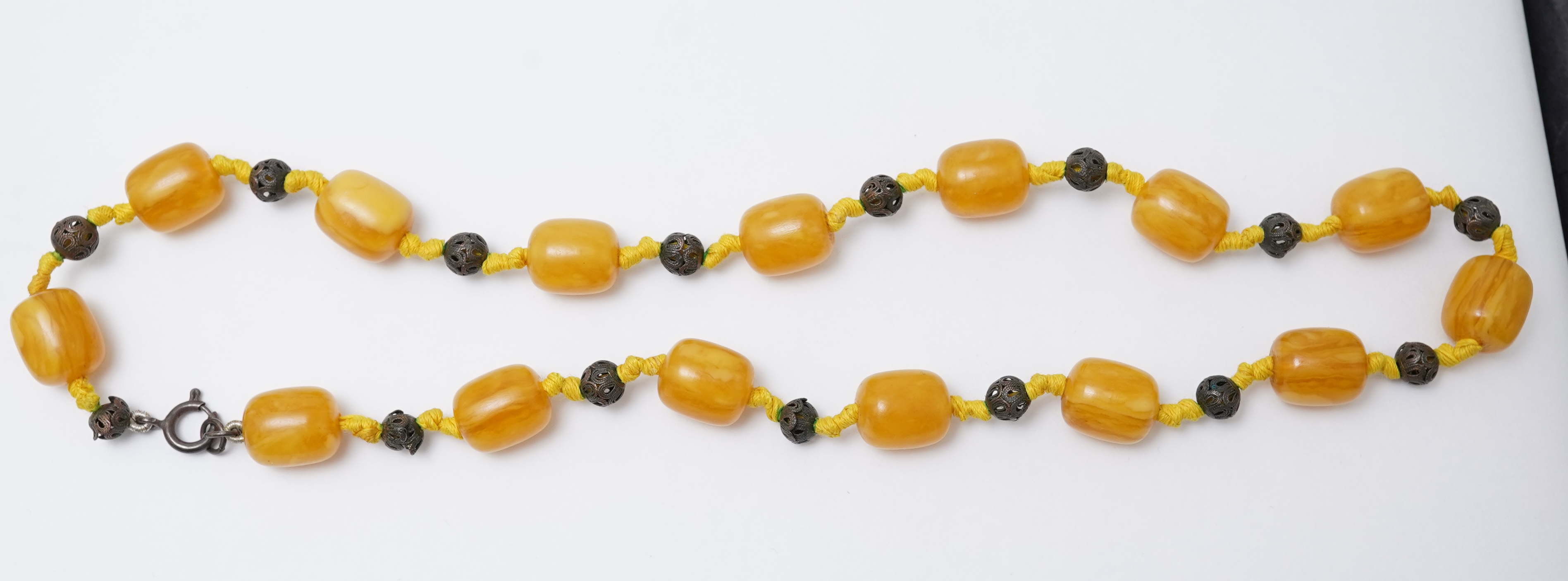 An amber necklace and carving, comprising: an amber necklace, composed of beads each measuring approximately 12 x 12 x 14mm, spaced by openwork metal beads, length 48cm; and an amber carving of a hawk on a rock, length 4
